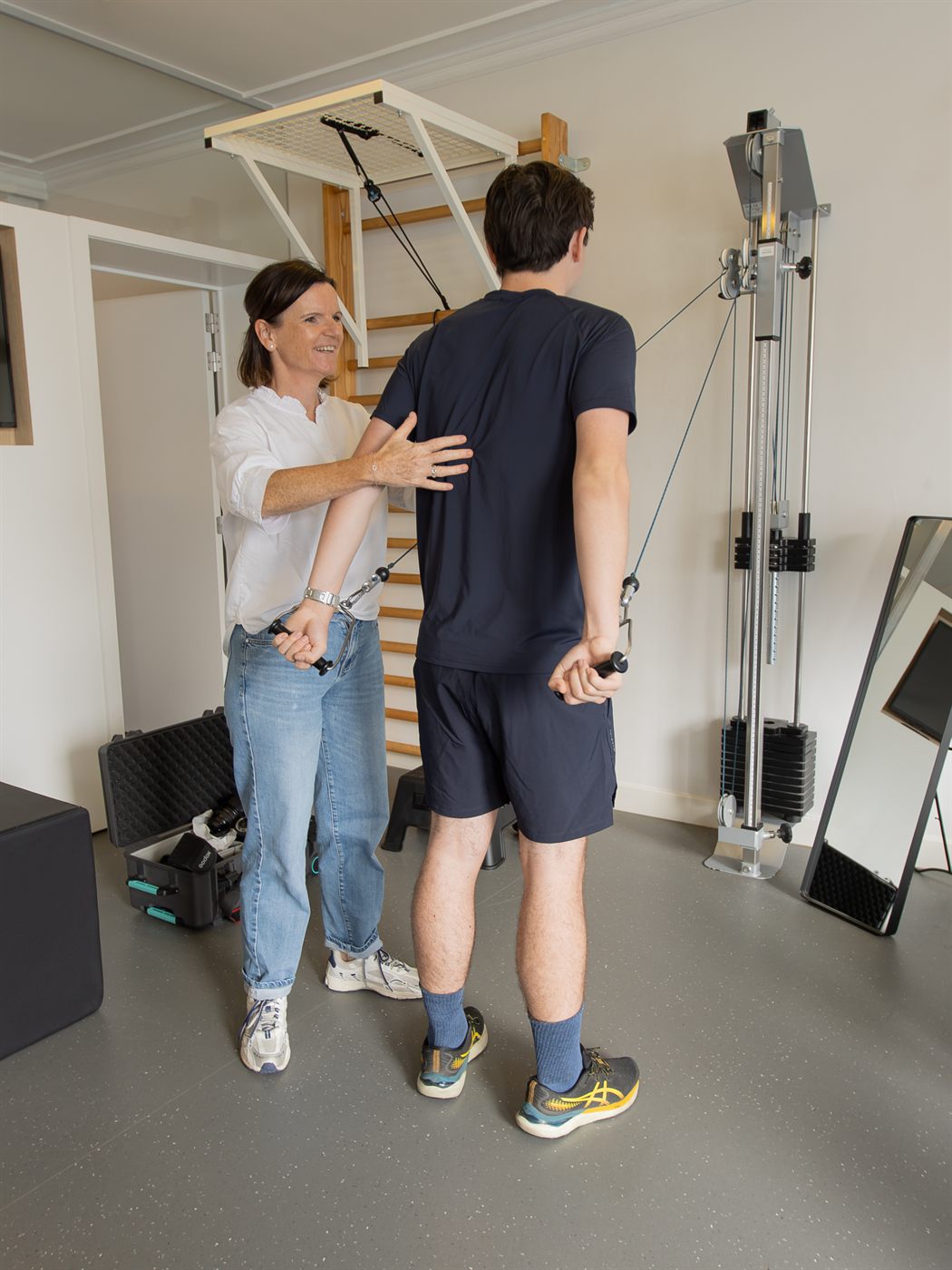 Kinesitherapeute begeleidt een patiënt bij krachttraining aan de kabeltoren